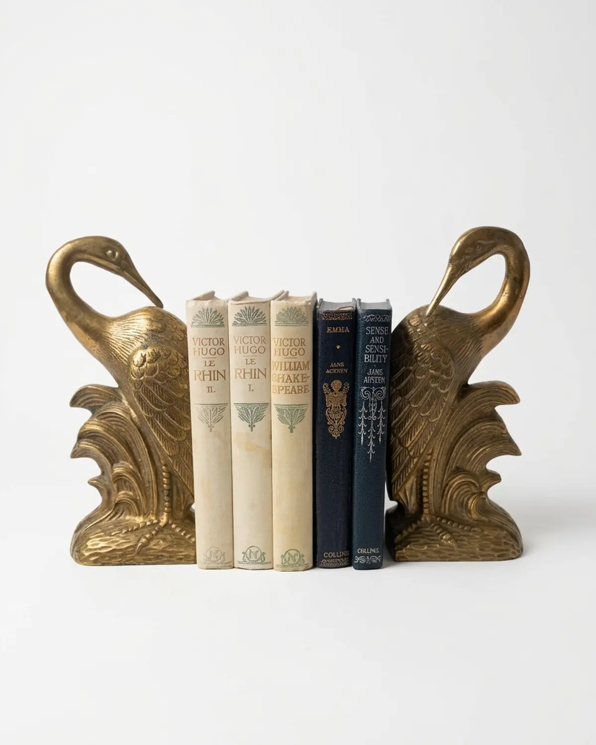 A pair of brass heron bookends holding vintage cloth-bound books on a mustard velvet cloth