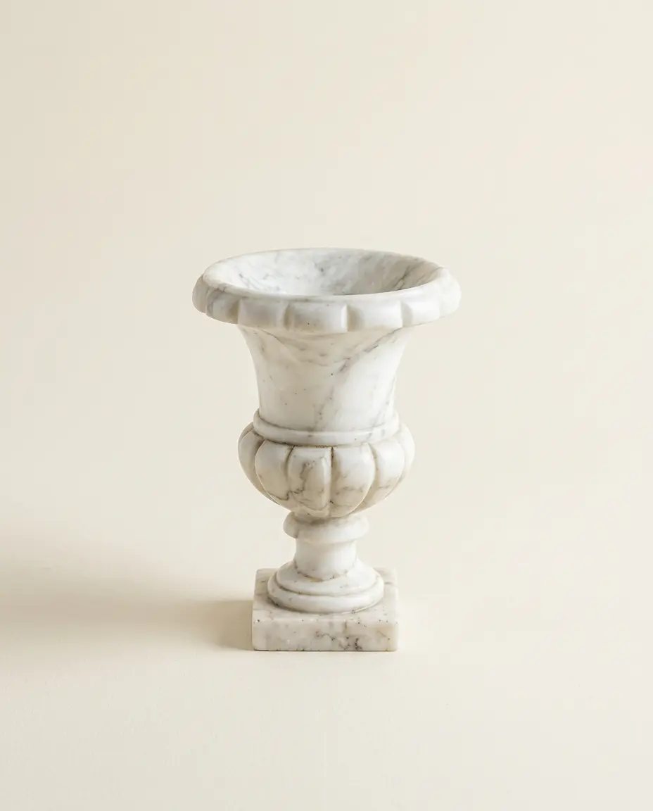 A small white marble urn with grey veining on a pale cream background